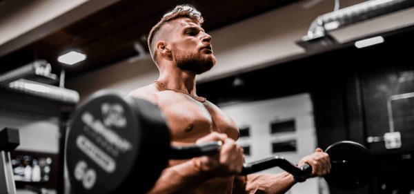A muscular man in a gym lifting a barbell with weights