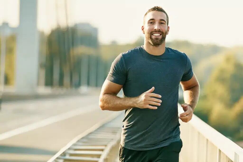 A man is running on a bridge, with a scenic view of the landscape in the background.
