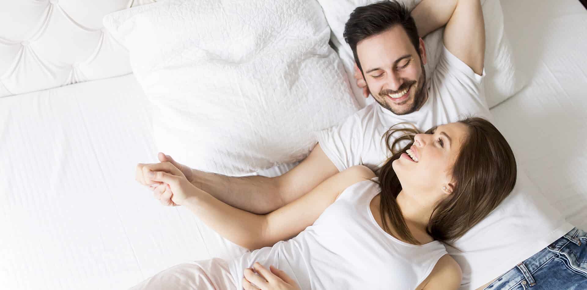 A man and woman lying together on a bed, appearing relaxed and comfortable in each other's company.